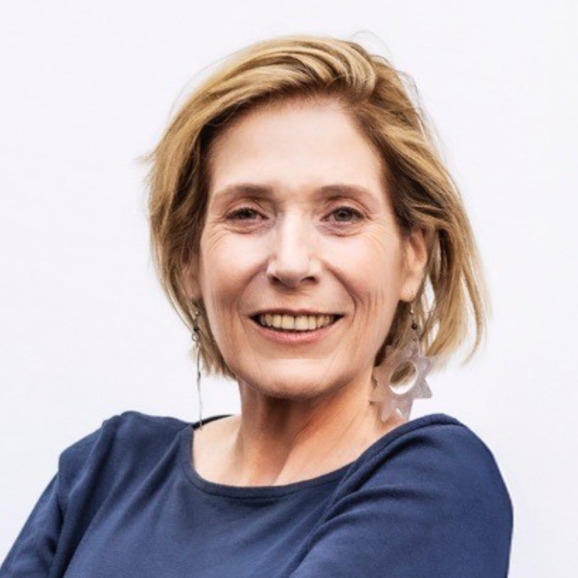 Headshot of white woman with short blonde hair wearing a dark blue top, looking at the camera and smiling